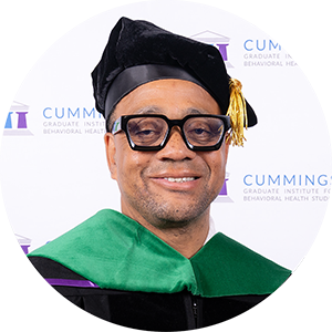 DBH graduate CDR Dr. Sean K. Bennett smiling in academic regalia and doctoral tam.